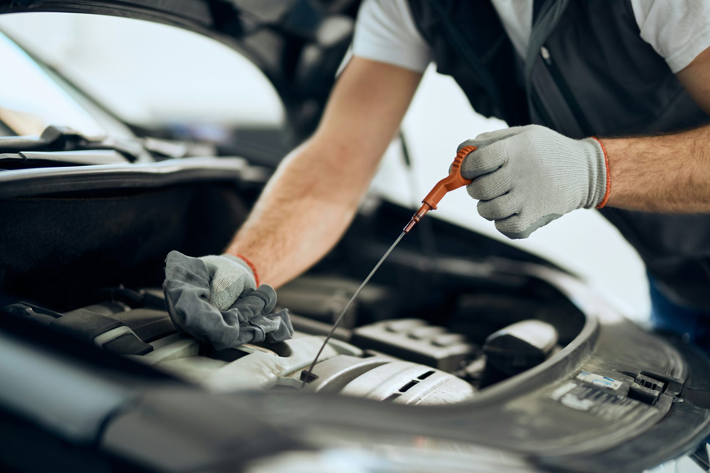 Gloved hands pulling the oil dipstick from a car engine to check the oil level
