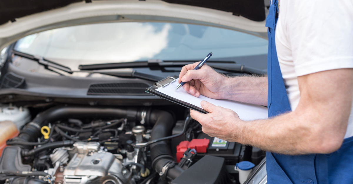 Mechanic writing on a clipboard beside a car with its hood open